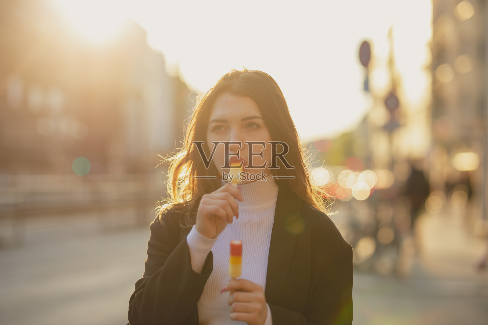 年轻女性在城市的道路上站着吃着风味冰淇淋，夕阳西下。照片摄影图片