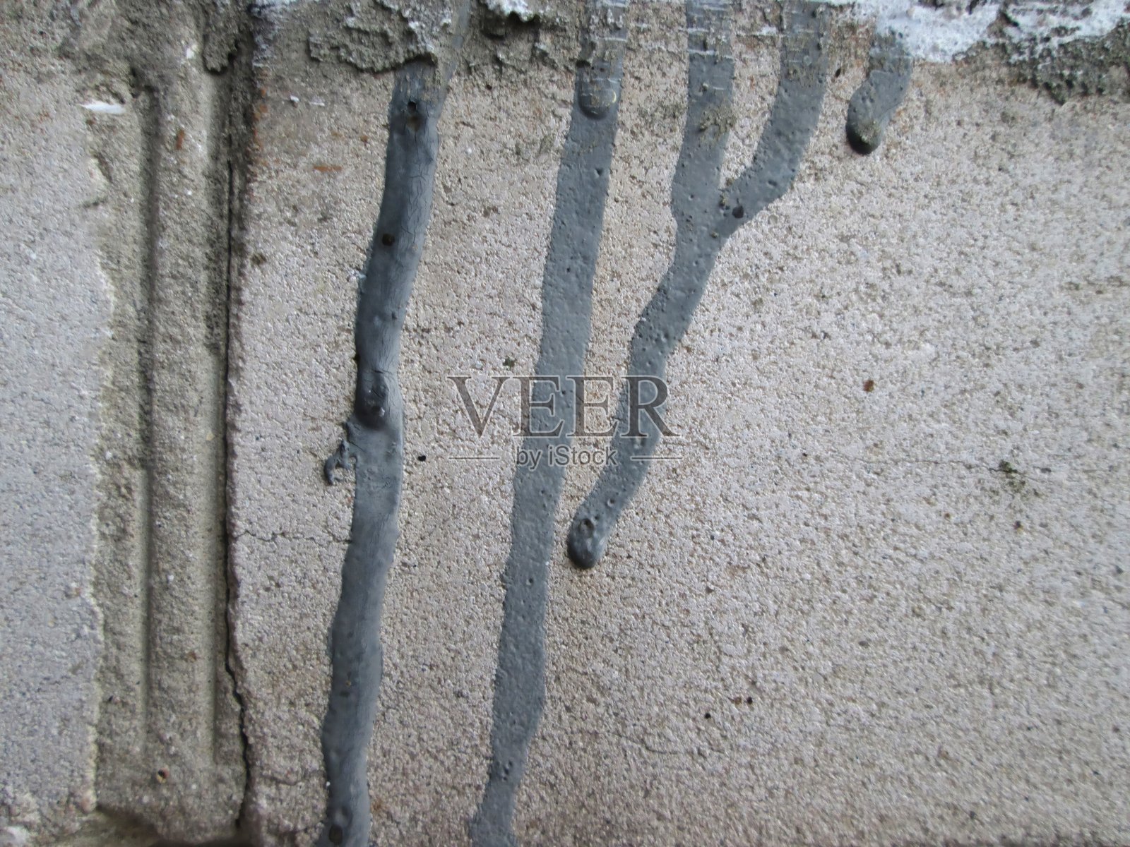 新鲜混凝土在白天的建筑工地上，从一面有纹理的墙壁上滴落成细流，展示了材料的流动性和施工过程。照片摄影图片