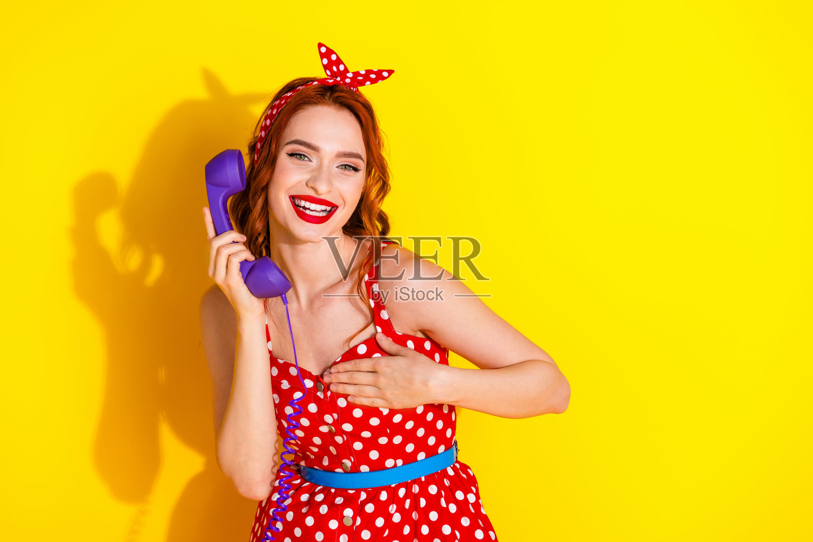 可爱的女孩穿着红色时尚连衣裙，独自在黄色背景下打电话，聊着新闻八卦秘密。照片摄影图片