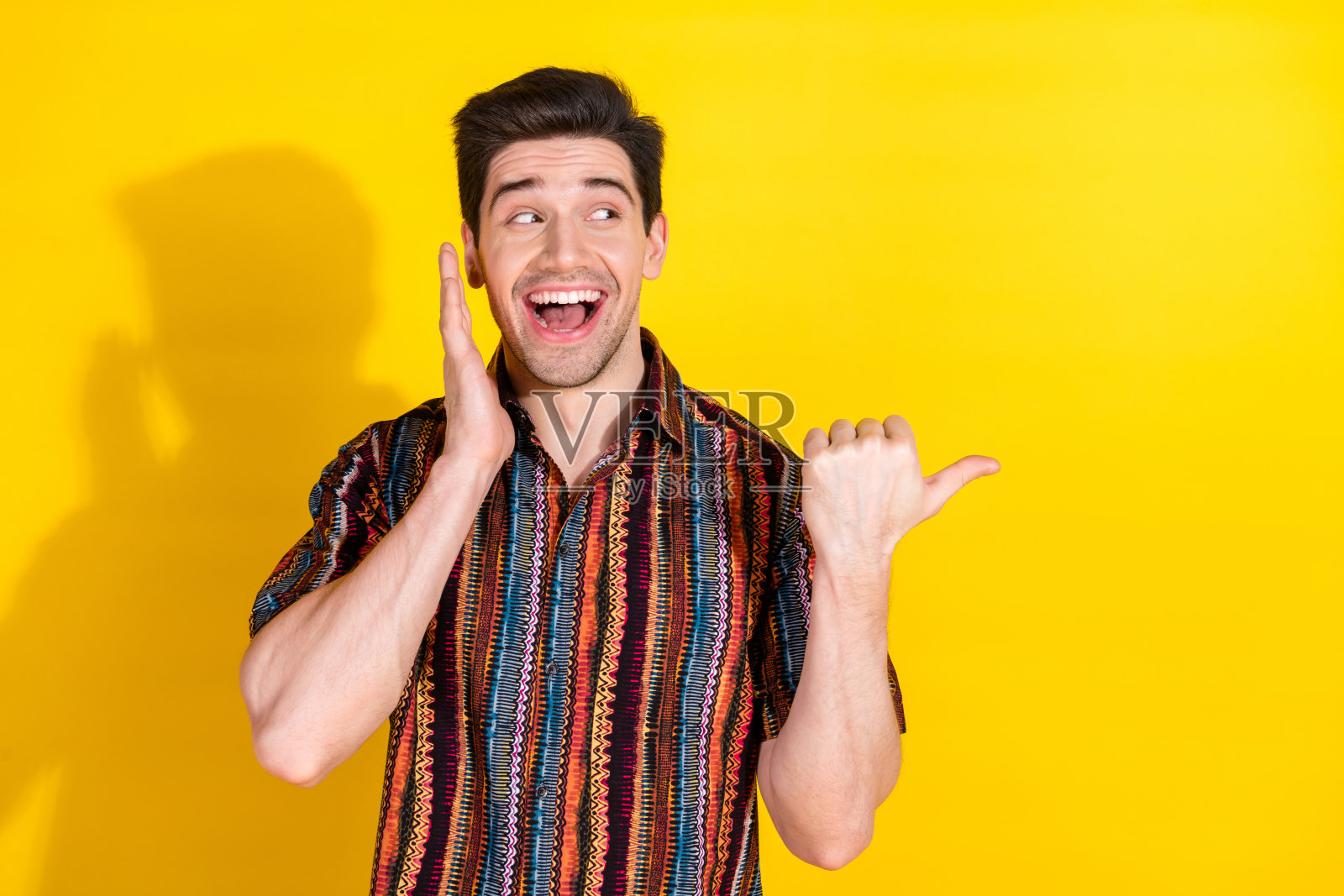 年轻男子的肖像，手指指向空白处，穿着衬衫，背景为黄色。照片摄影图片