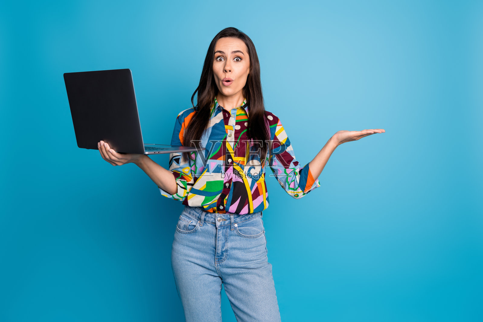 直发女孩的肖像，手持笔记本电脑，空着手掌展示物体，背景为蓝色。照片摄影图片