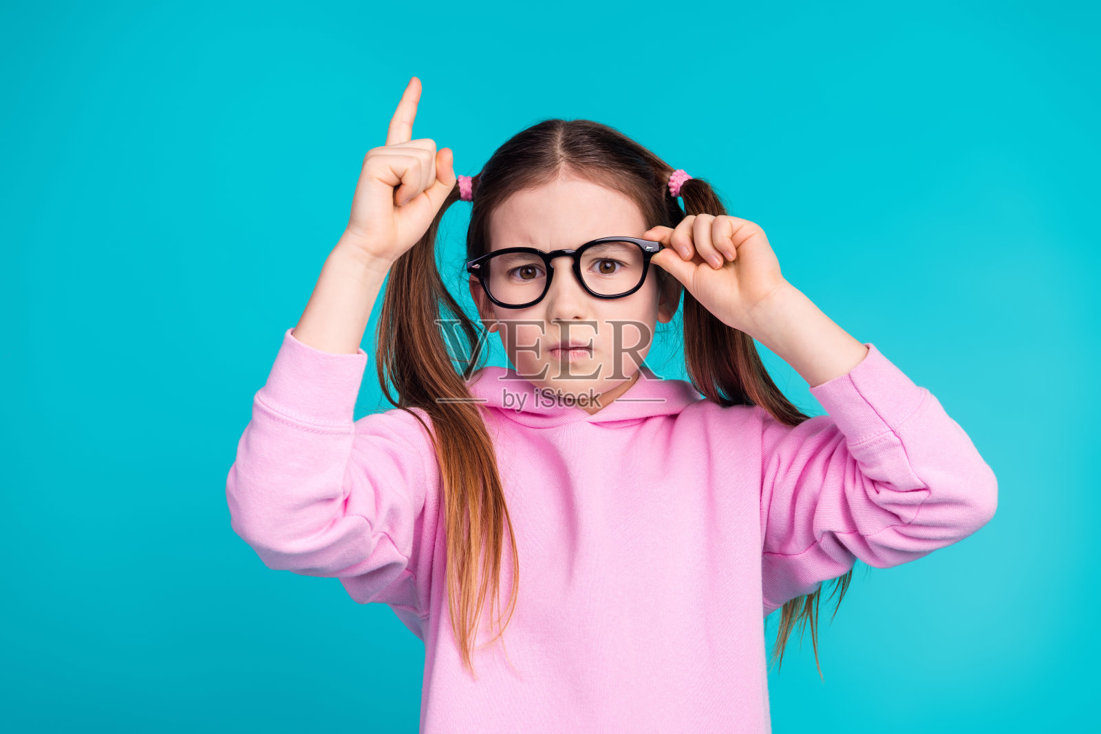 可爱的小女孩触摸眼镜，兴奋地穿着时尚的粉色衣服，背景为水绿色。照片摄影图片