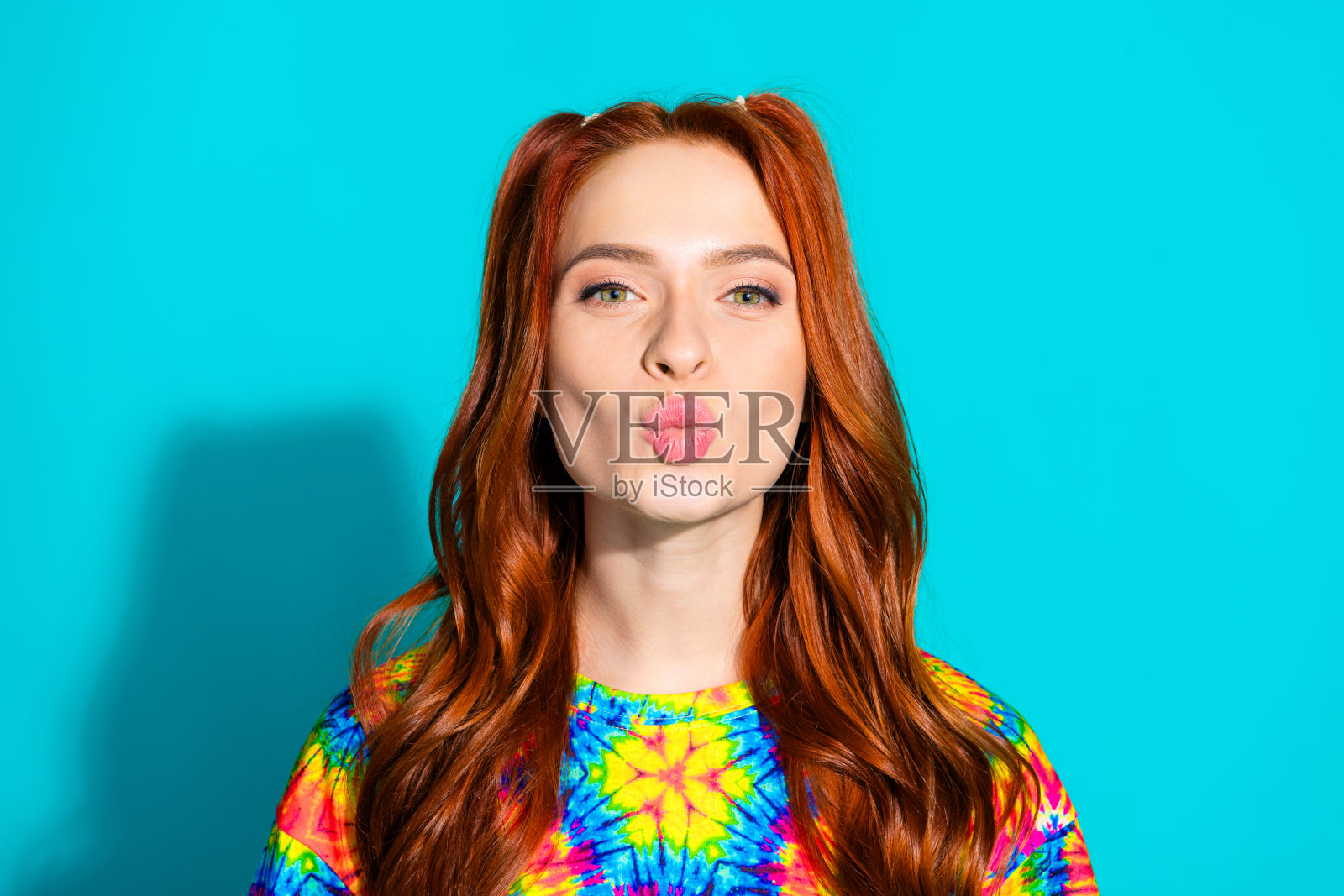 年轻女士的照片肖像，亲吻嘴唇，穿着时尚多彩的服装，背景为青色。照片摄影图片