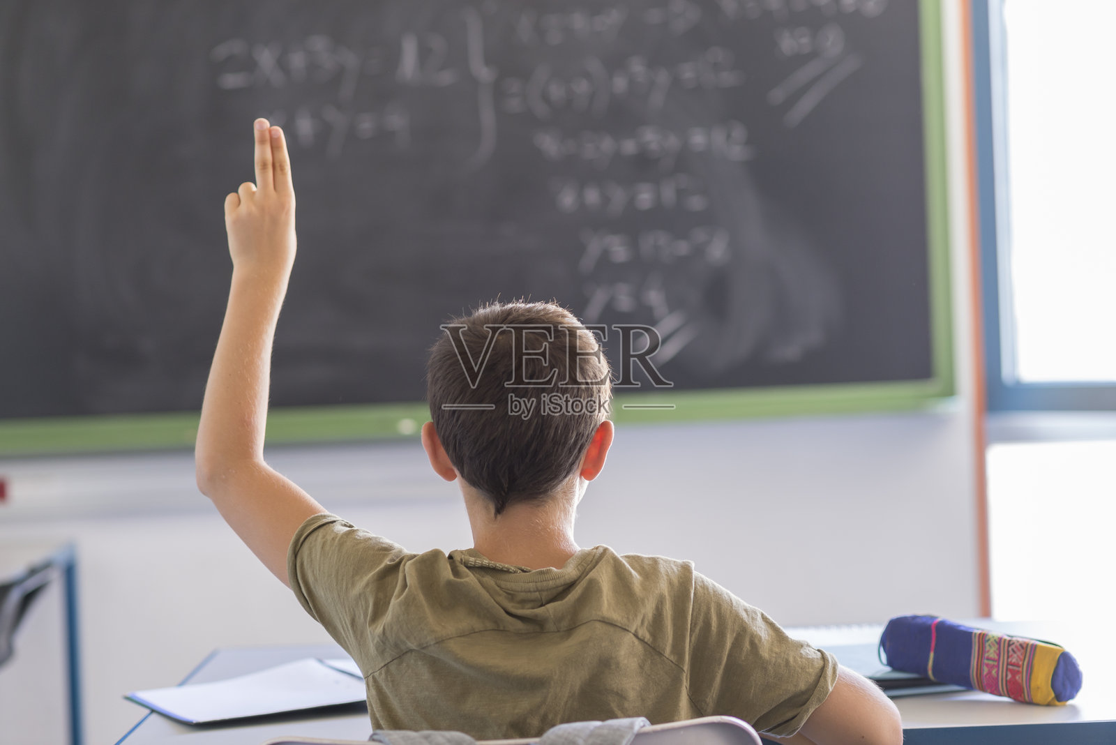 教室里坐着的男孩背影，手举起。照片摄影图片