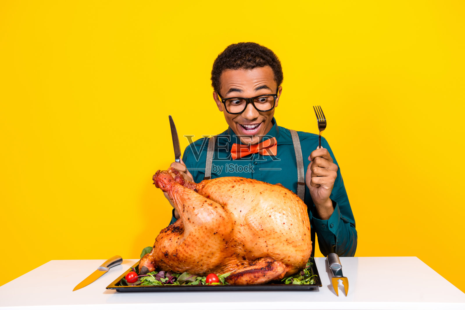 惊讶的男士坐在桌前，兴奋地举起餐具享用感恩节大火鸡，背景色彩鲜艳。照片摄影图片