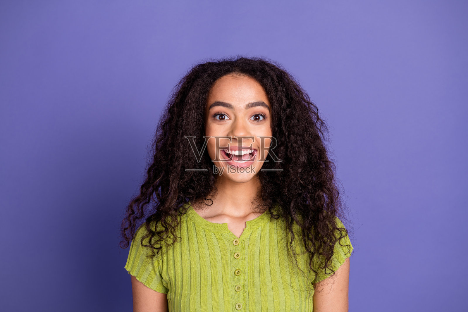 时尚穿着绿色衣服的迷人少女，兴奋地看着镜头，背景为紫色。照片摄影图片