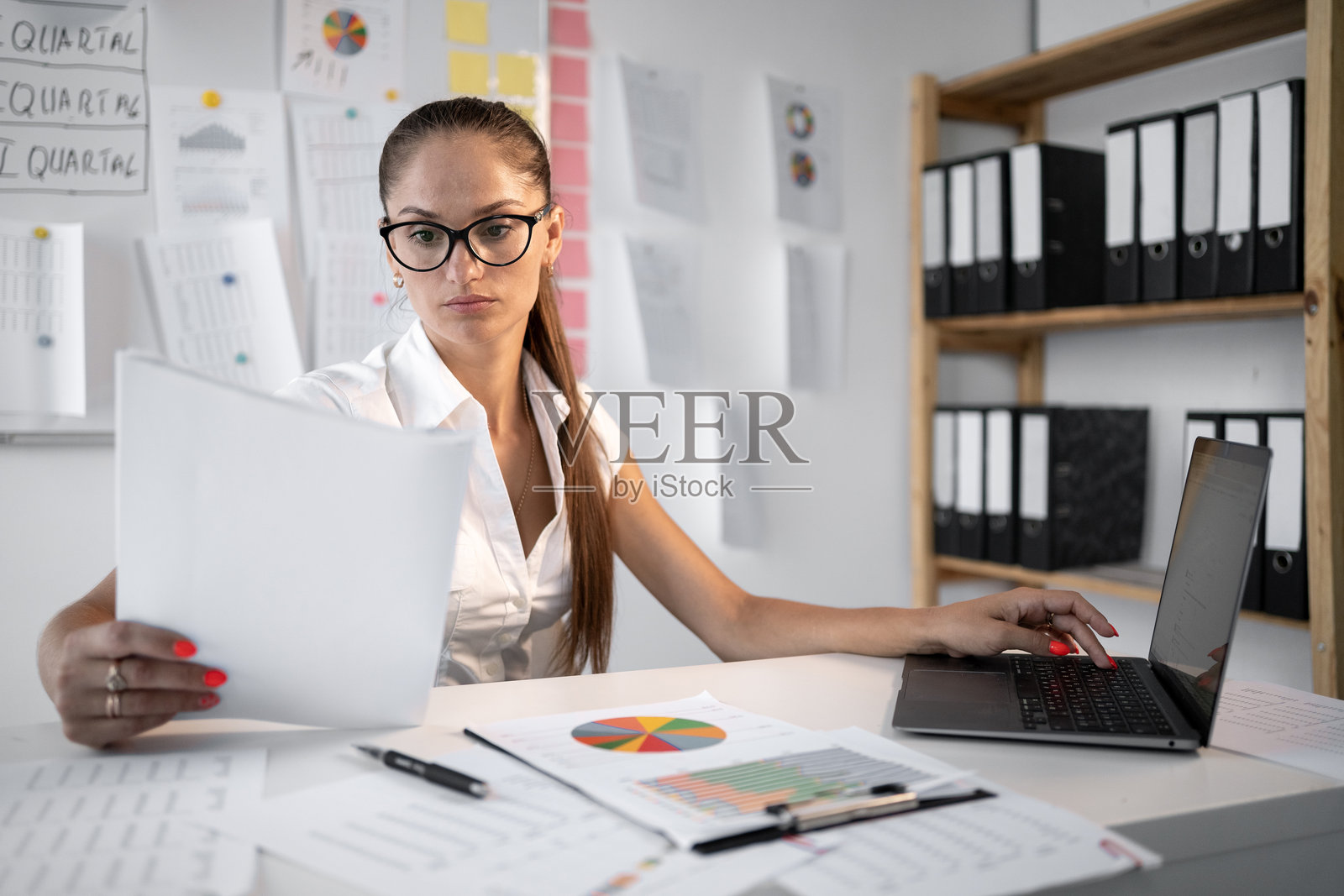 在办公室使用文件和笔记本电脑的女商人。会计在签字前分析合规和审批文件照片摄影图片