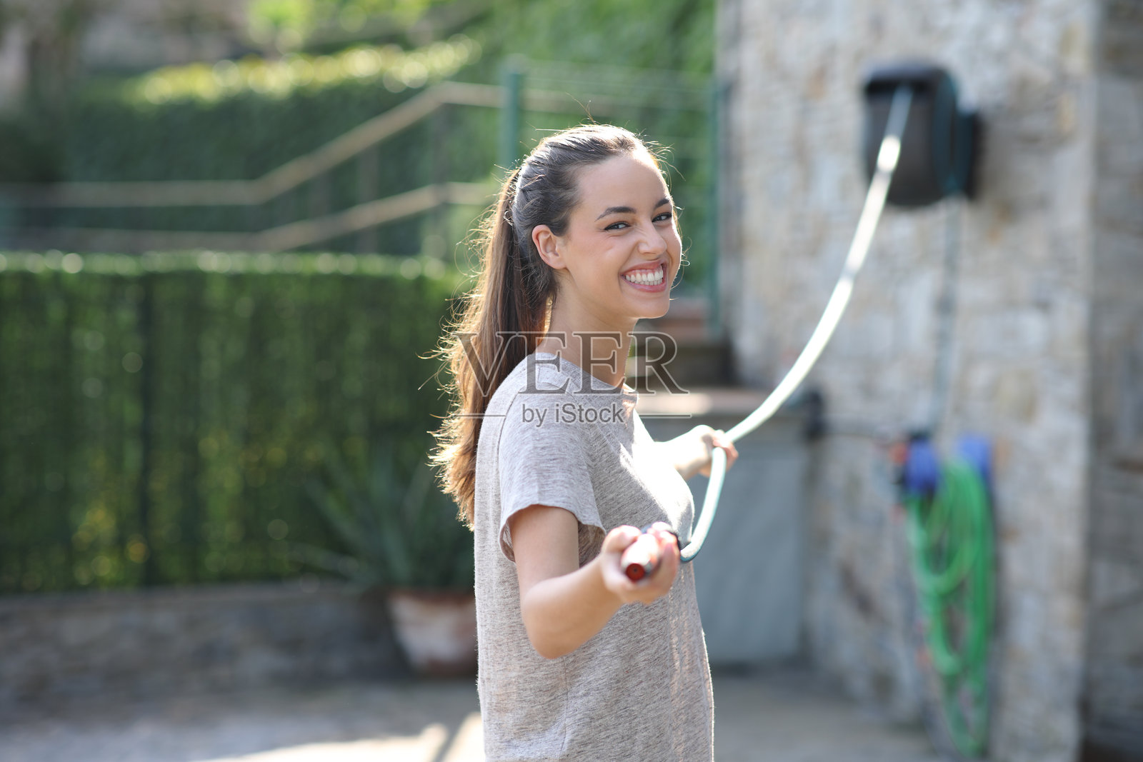 快乐的女人在花园里展开软管照片摄影图片