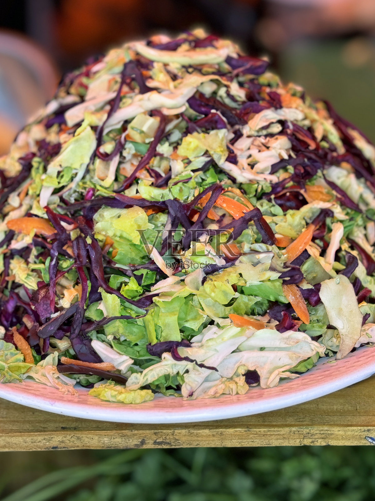 粉色图案的餐盘上盛放着一堆卷心菜和胡萝卜的沙拉混合物，特写镜头展示了切好的蔬菜、刨丝的胡萝卜和切片的卷心菜，背景是市场摊位，焦点在前景。照片摄影图片