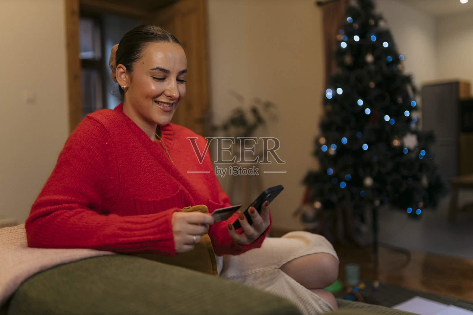 放松的年轻女性正在使用手机和信用卡进行圣诞节的在线购物照片摄影图片
