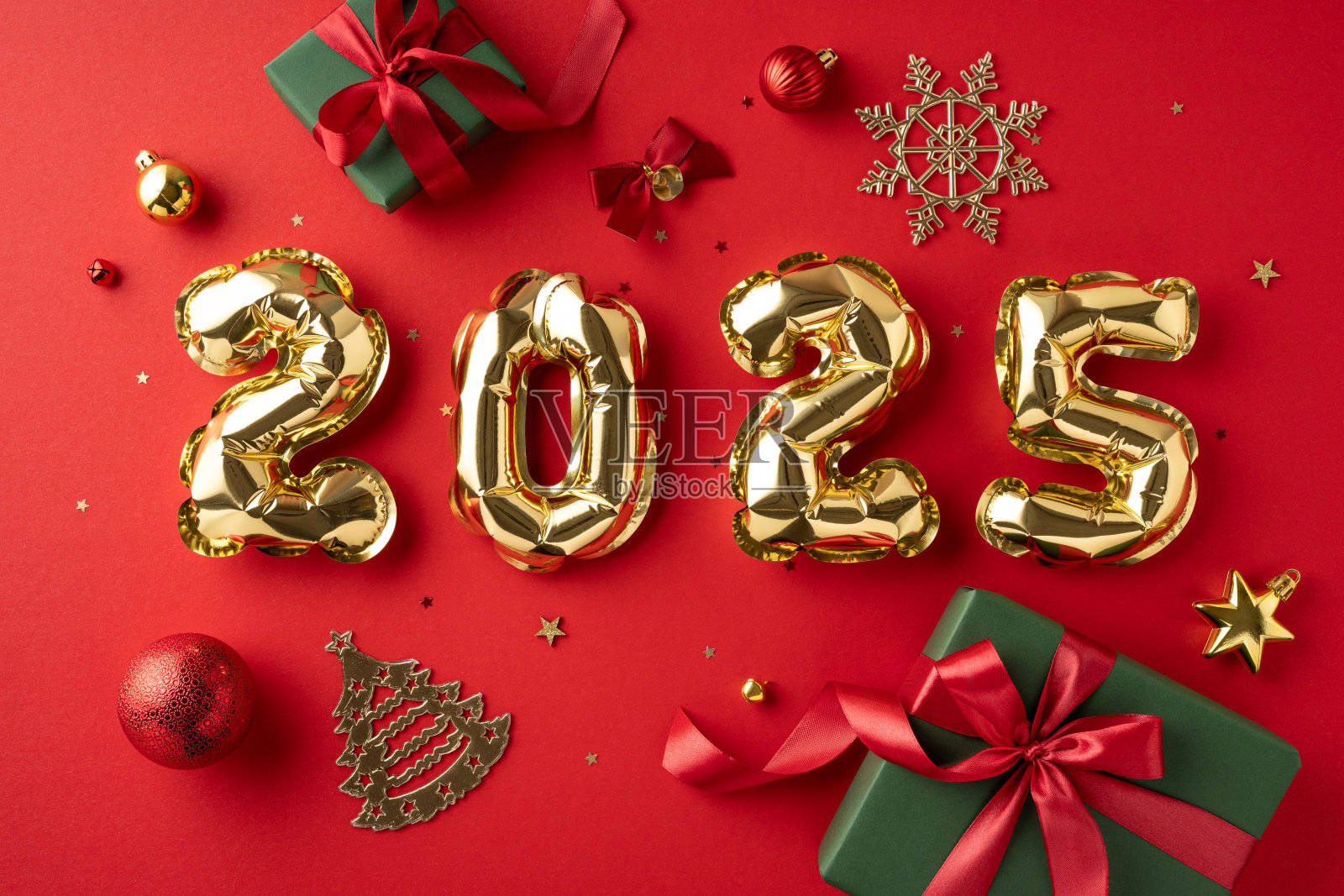 红色背景上有2025的金色气球数字，周围装饰着圣诞装饰品和礼物，象征着节日的新年庆祝活动。照片摄影图片