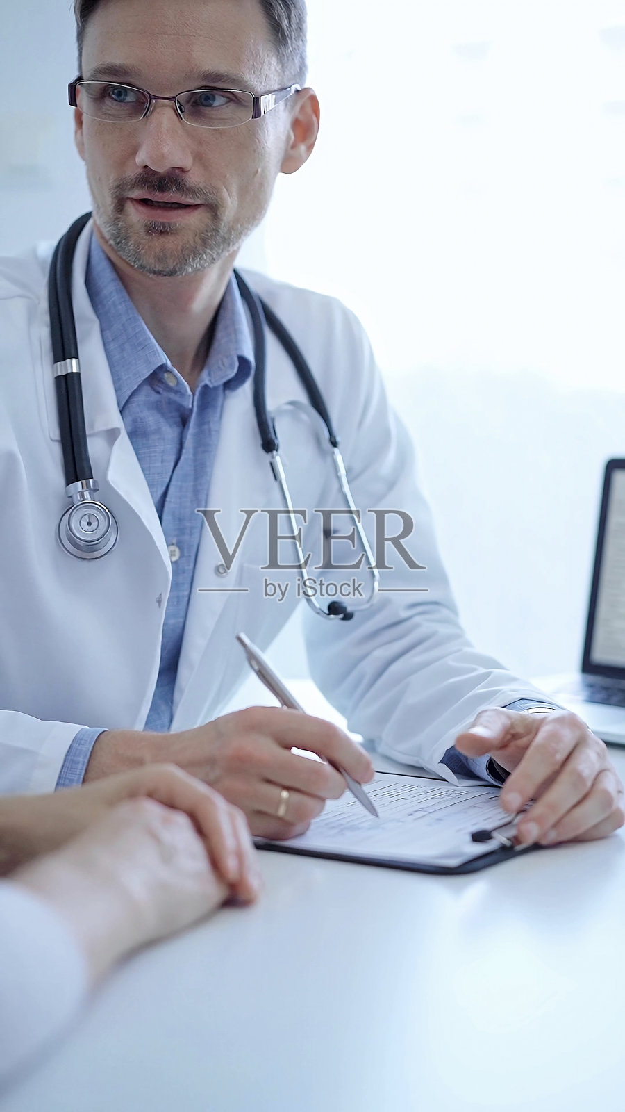 医生和病人：医生穿着白色医用外套和蓝色衬衫，在诊所咨询期间用手势示意，医学概念照片摄影图片