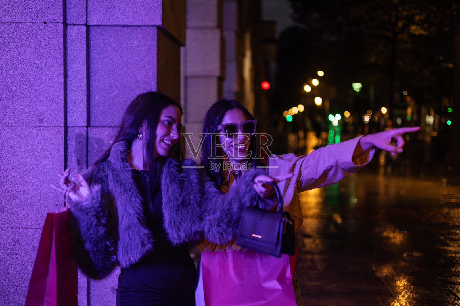 在一个下雨的夜晚，微笑的拉丁裔朋友在购物时用手指指着，手里拿着纸袋照片摄影图片