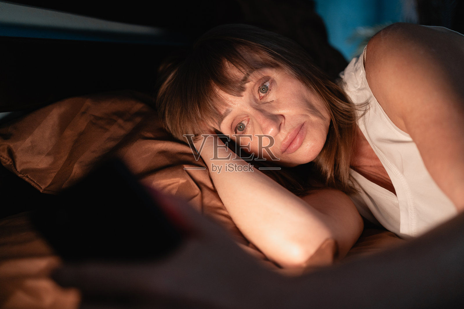 晚上醒来在床上玩手机的困倦女人照片摄影图片