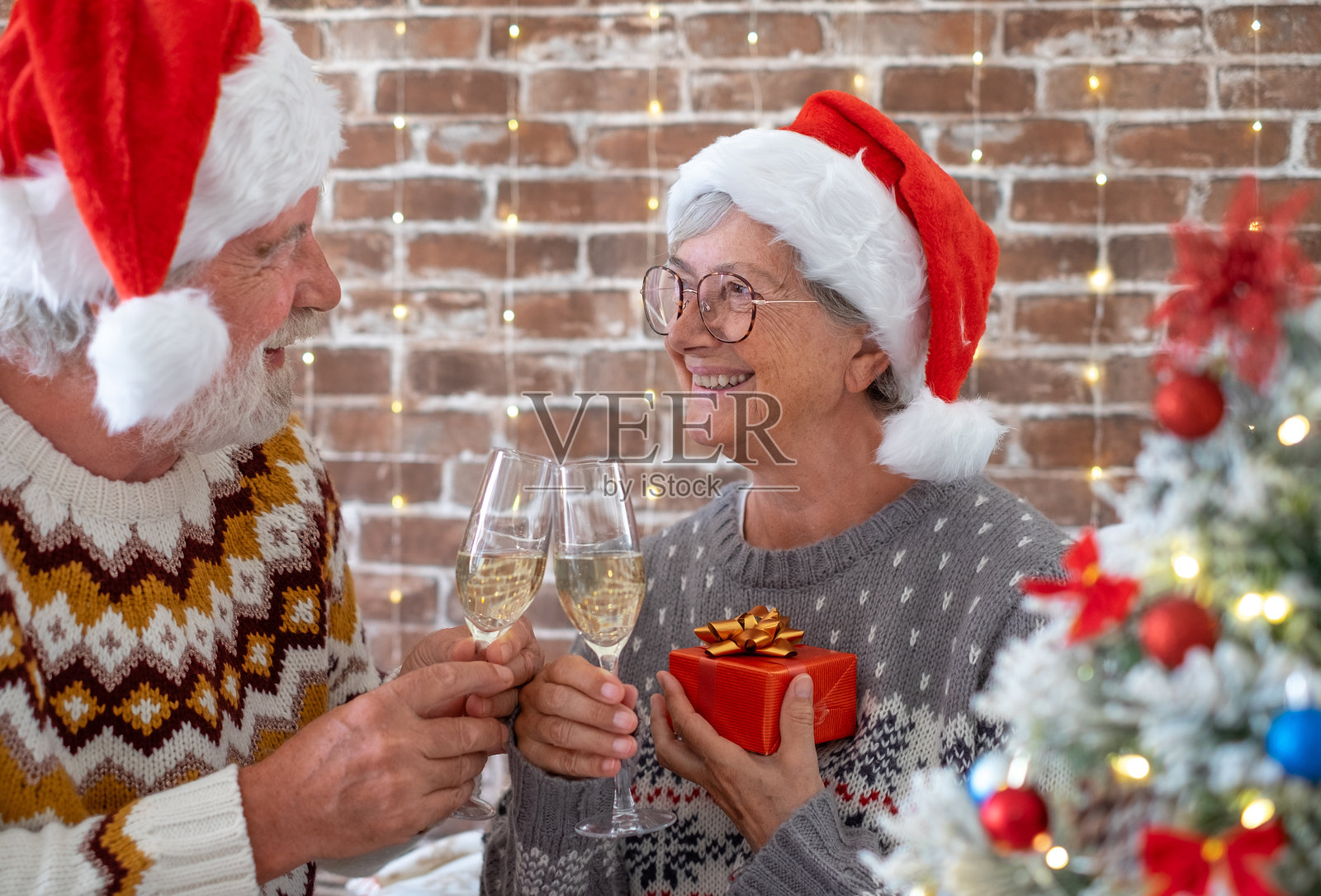 快乐的老年夫妇在十二月一起享受圣诞假期，戴着圣诞老人帽。男女举杯祝酒，互相凝视。照片摄影图片