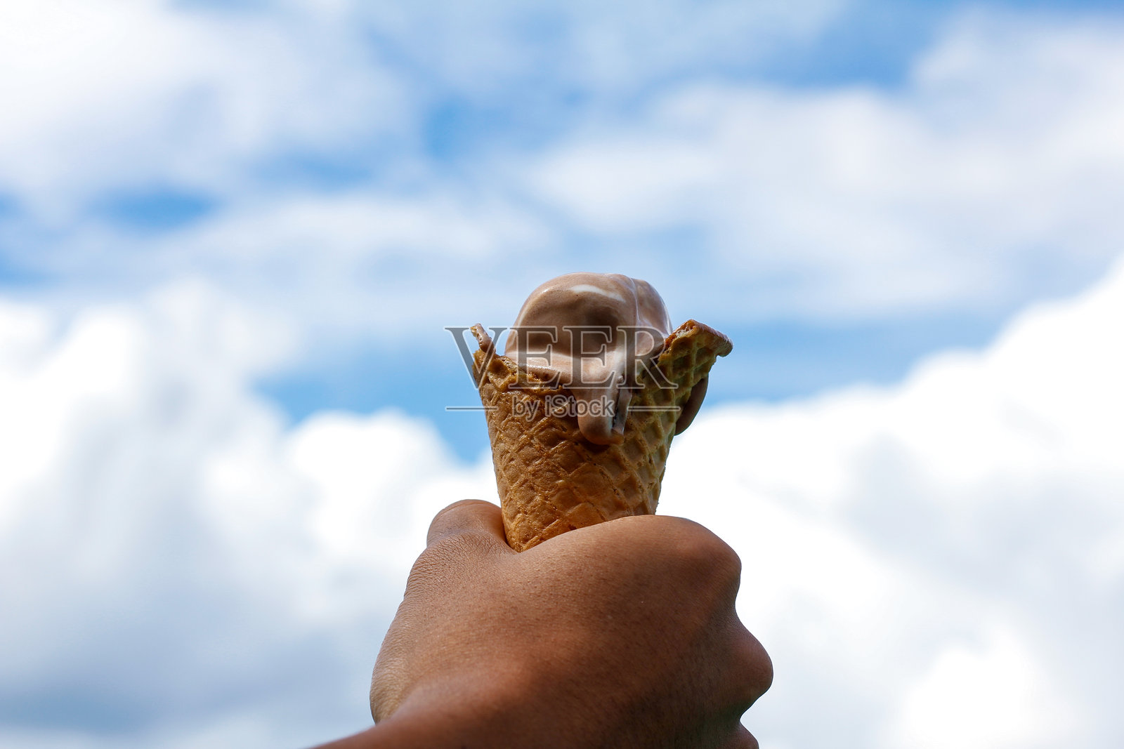 男人的手握着冰淇淋，背景是云朵。照片摄影图片