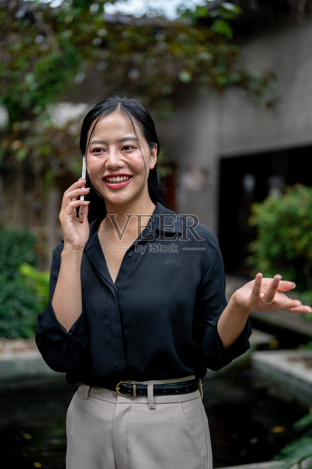 一位迷人的亚洲女商人在花园中放松时与人通话。照片摄影图片