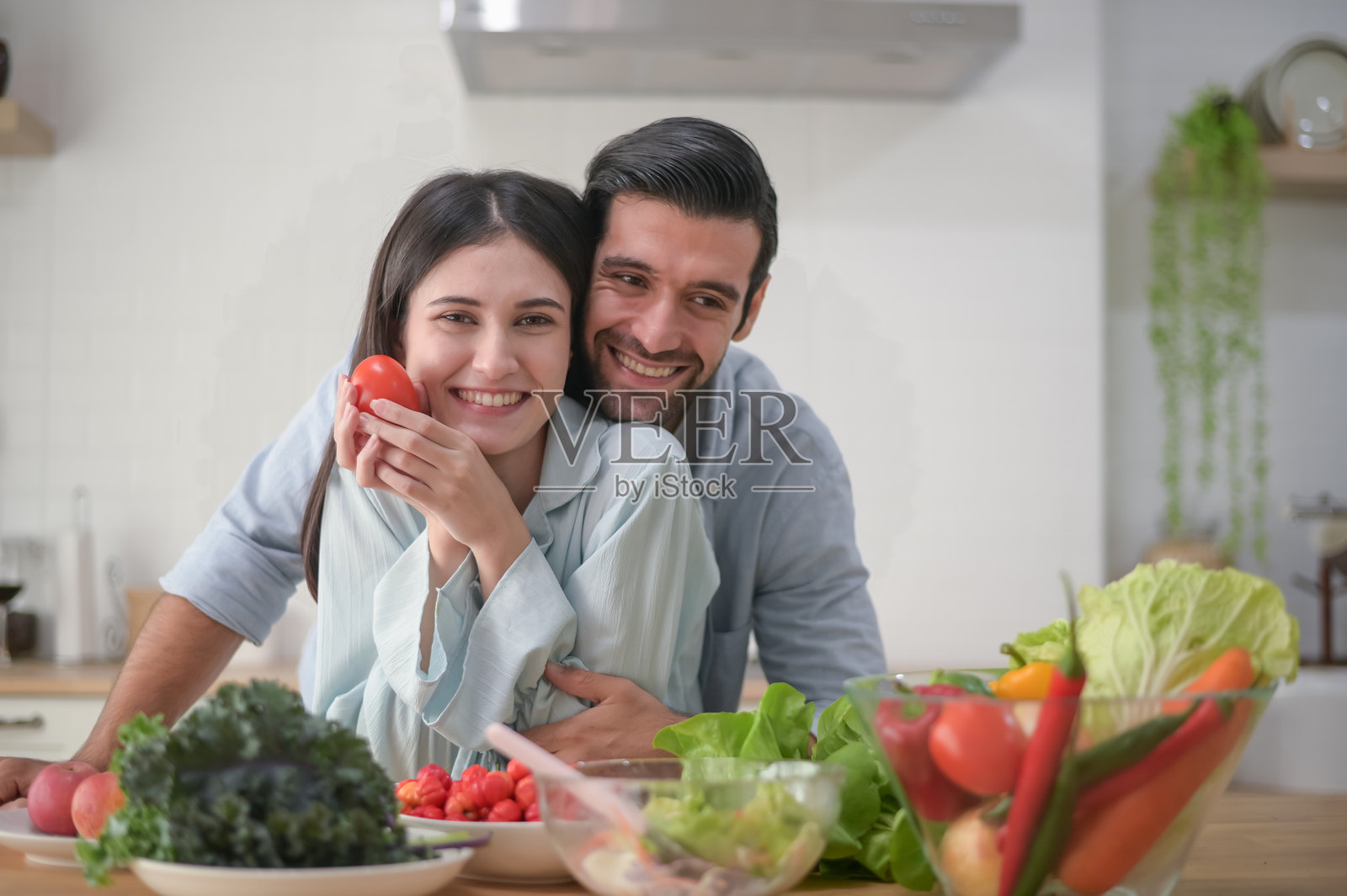 快乐的情侣在家准备食物，厨房台面上摆放着各种新鲜的蔬菜沙拉照片摄影图片