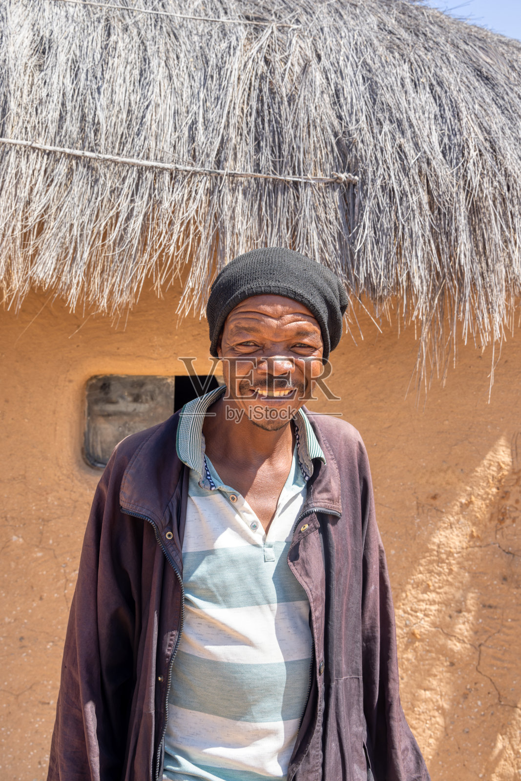 非洲村庄：站在茅草泥屋前的胡须男子，在小镇里照片摄影图片