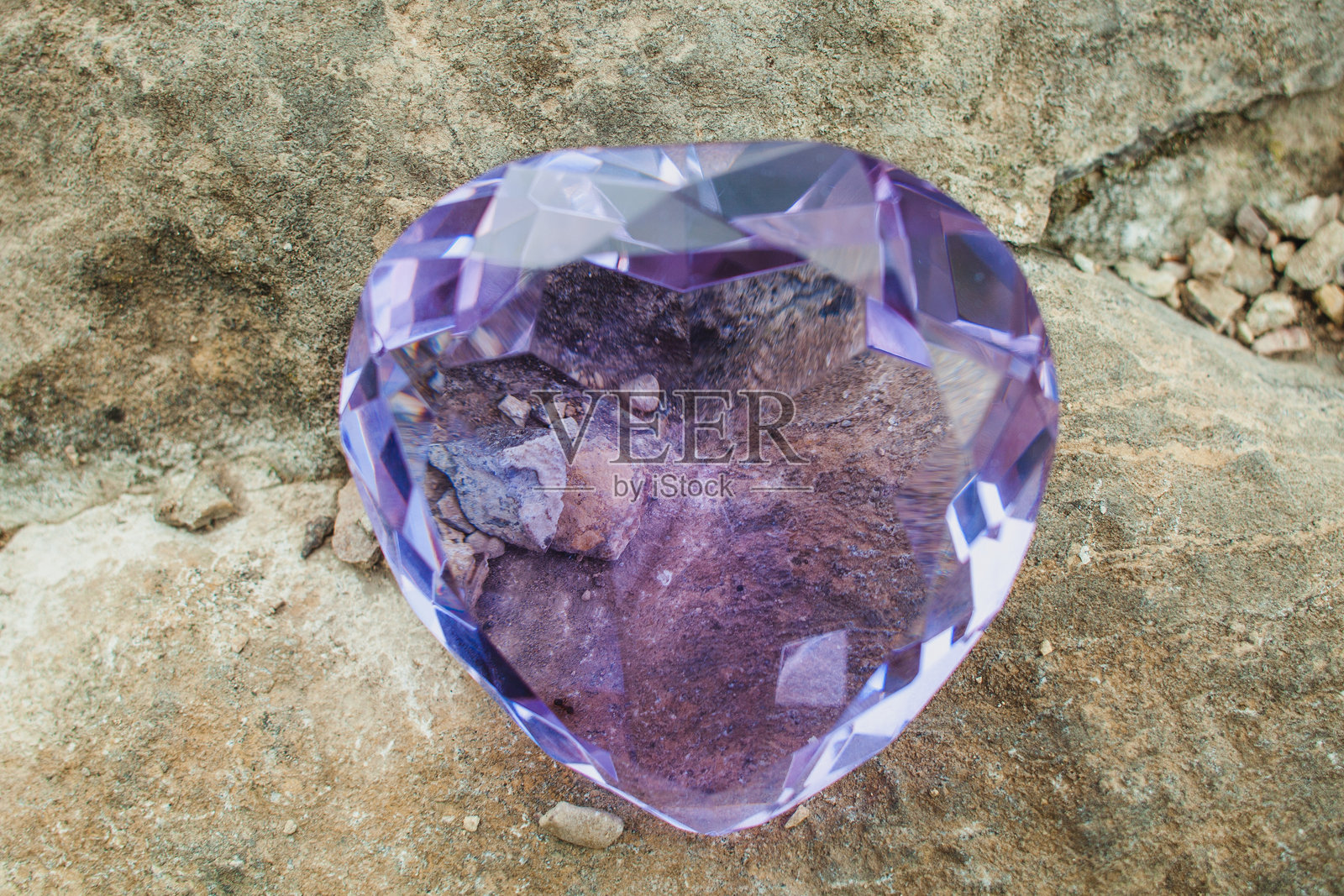 一颗璀璨的紫色切割水晶静静地躺在背景中的岩石上。照片摄影图片