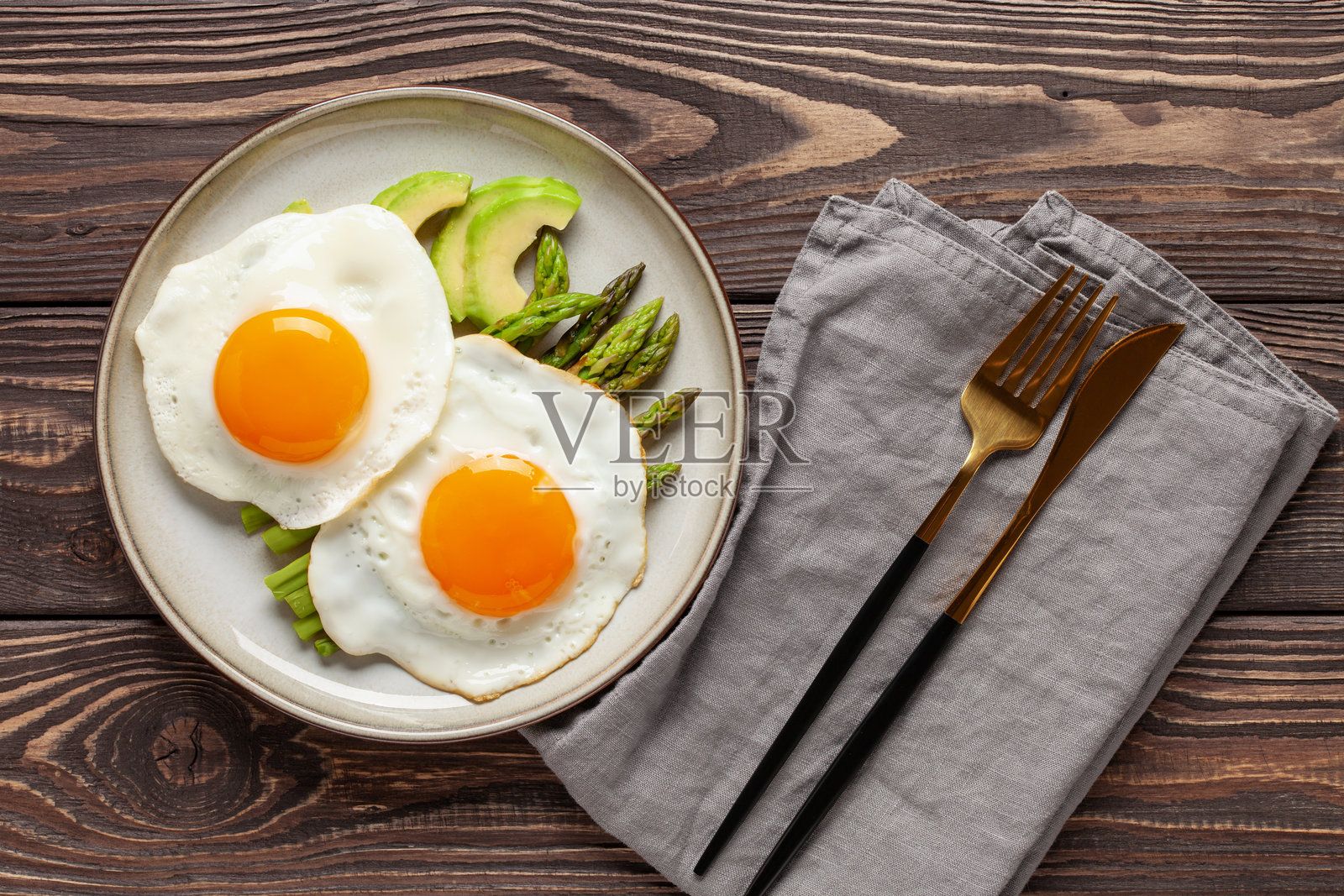 美味的早餐。盘子里有煎蛋、绿芦笋和鳄梨，放在木桌上。俯视图。照片摄影图片
