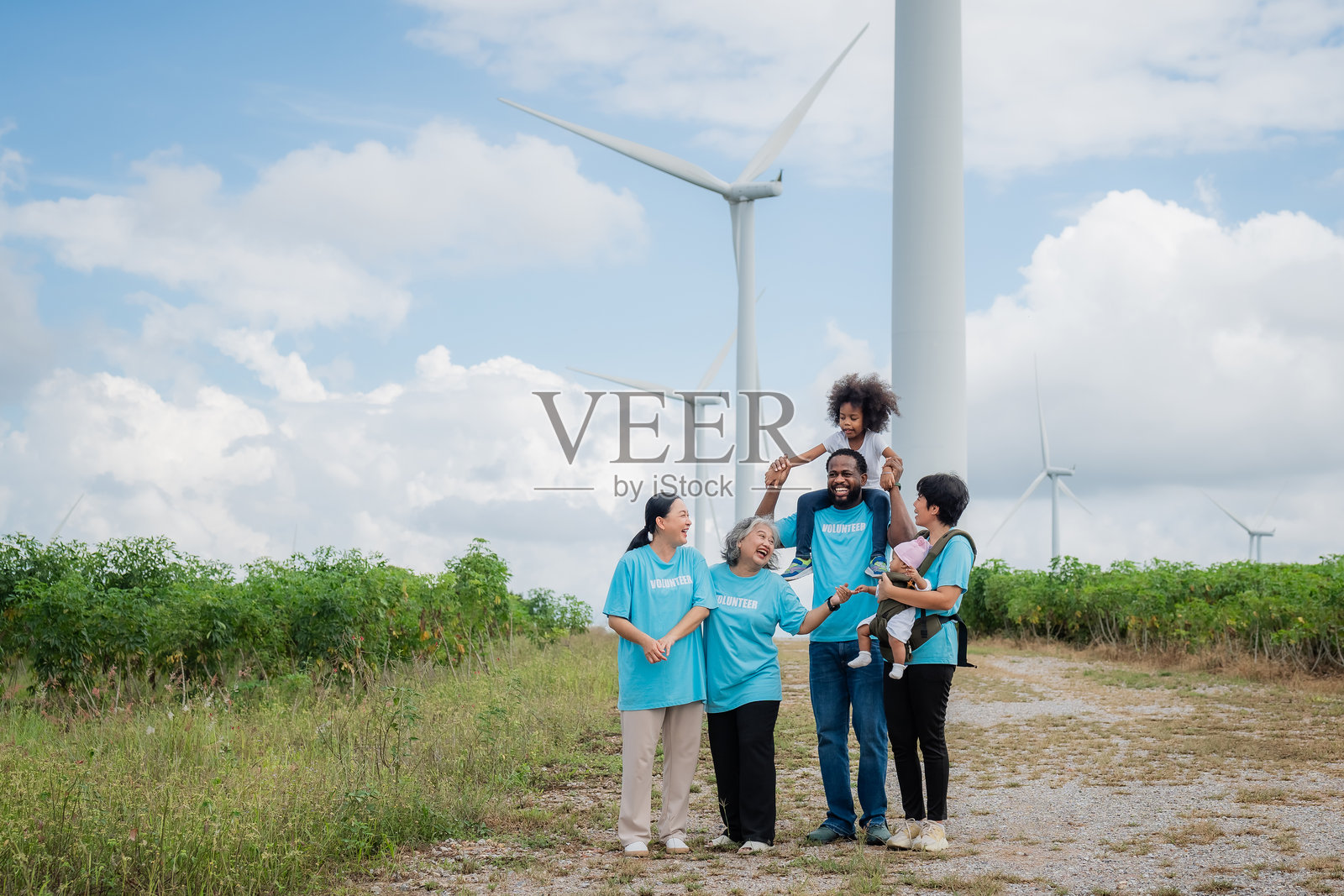 一家五口站在风电场前，其中一个孩子被一名男子抱着。环境，清洁，风力涡轮机，志愿者，社区，团队合作，社会，关爱，自然照片摄影图片
