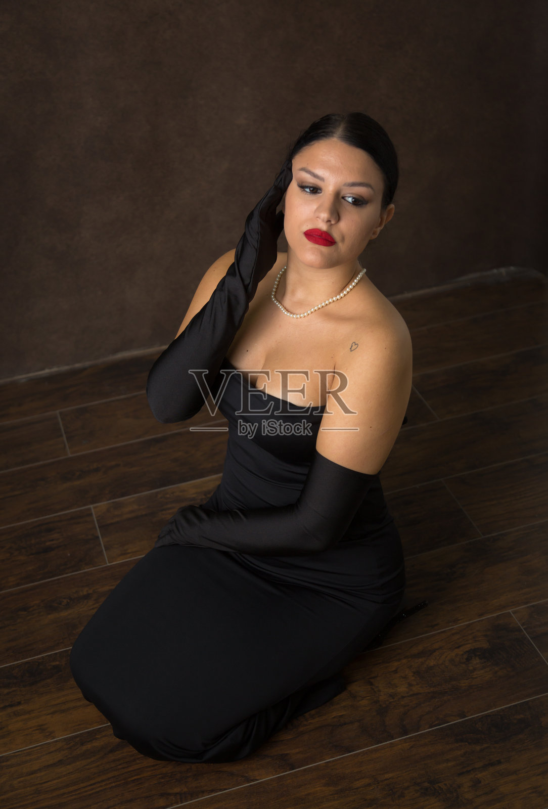 在摄影棚灯光下，她的红唇和黑色服装与深棕色背景形成鲜明对比。照片摄影图片