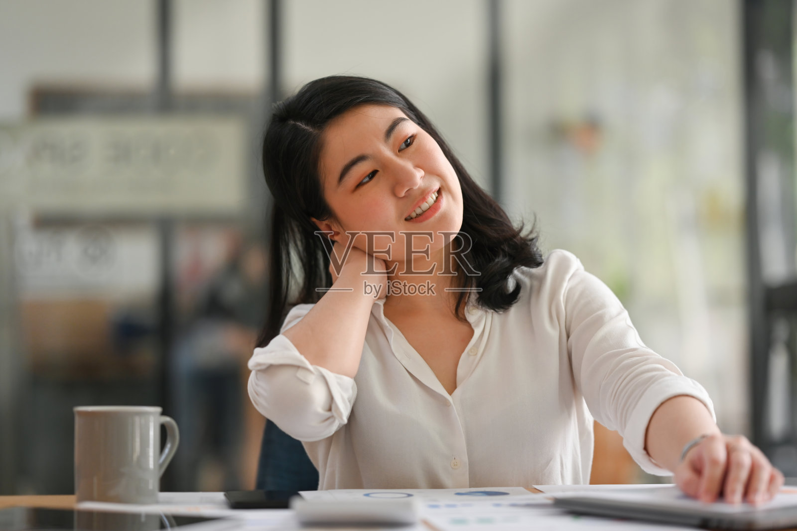 年轻亚洲女商人或女办公室工作人员在工作时伸展脖子，工作间歇期间自我拉伸以减少办公室综合症的发生。照片摄影图片