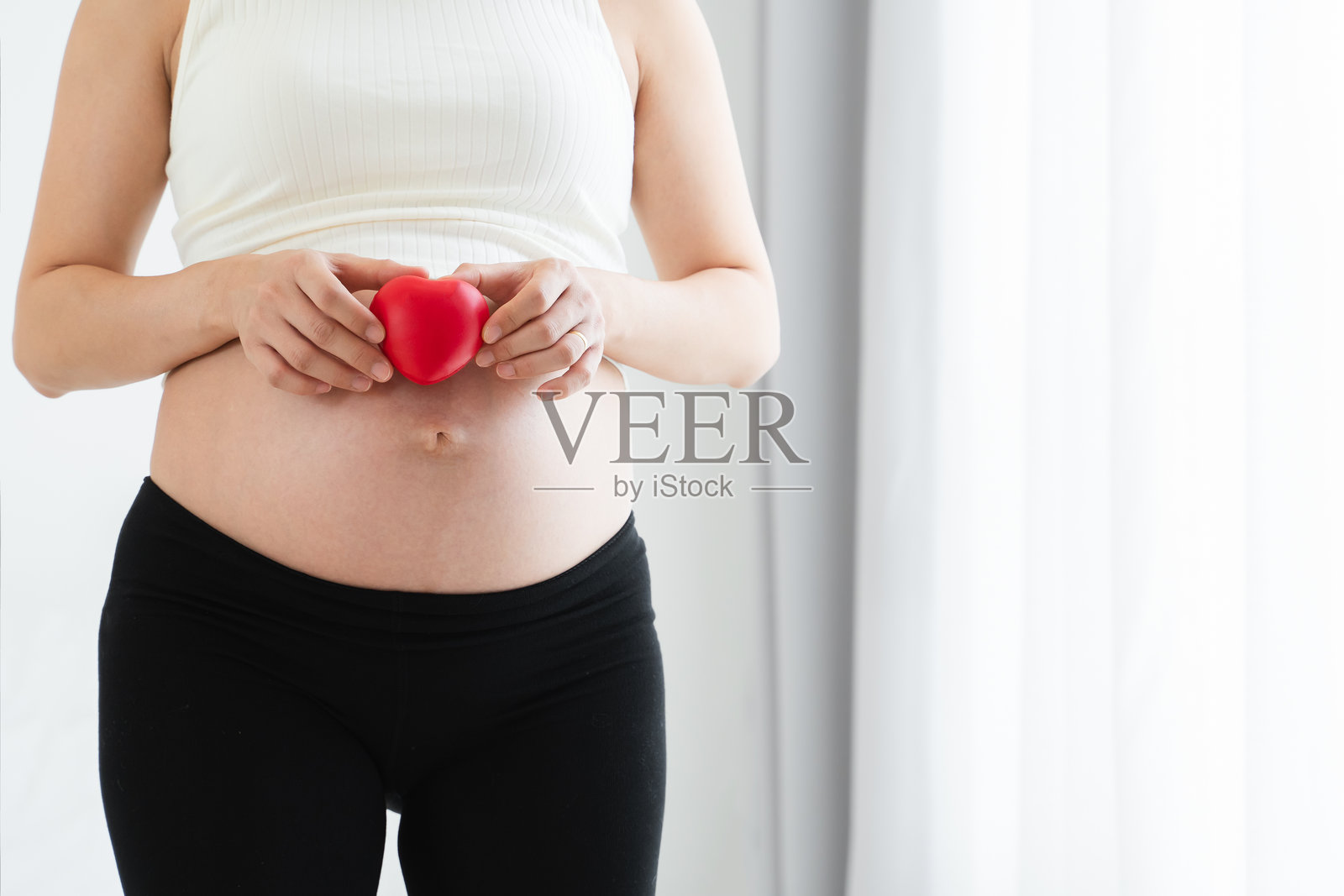 亚裔孕妇手捧红心玩具，呵护腹中胎儿照片摄影图片