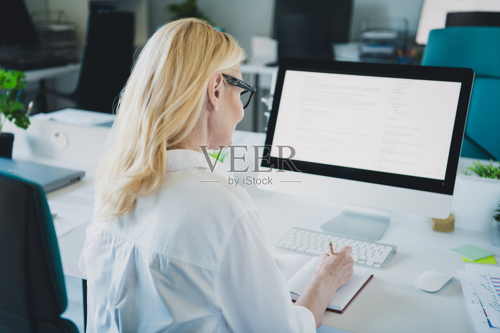 成功女性的商务秘书，金发，穿着正式的白衬衫，专注于电脑屏幕，记录日记。照片摄影图片