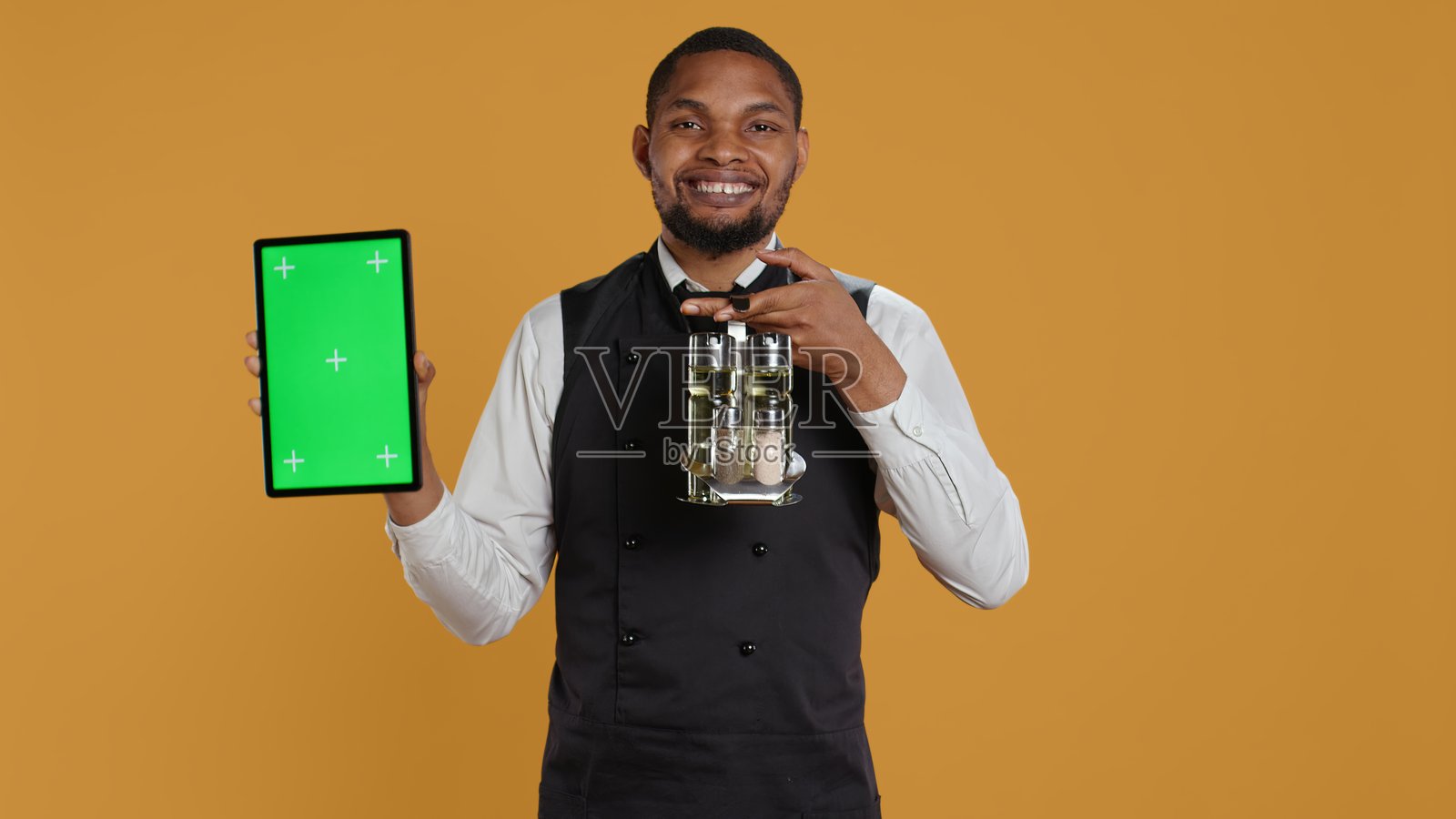 餐厅工作人员在黄色背景下展示带有绿色屏幕的平板电脑照片摄影图片
