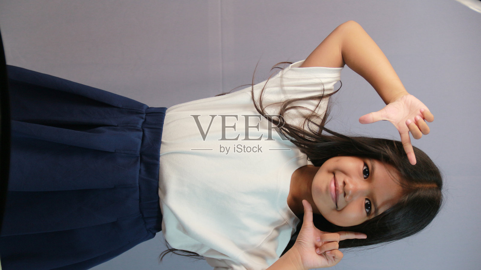 自信的亚洲儿童穿着白色T恤在灰色背景前摆姿势照片摄影图片