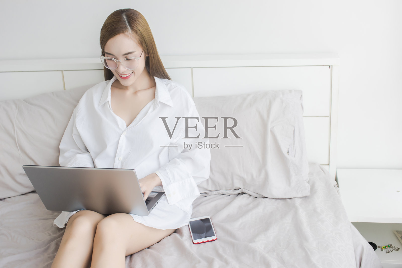 年轻女性坐在家里的床上使用笔记本电脑照片摄影图片