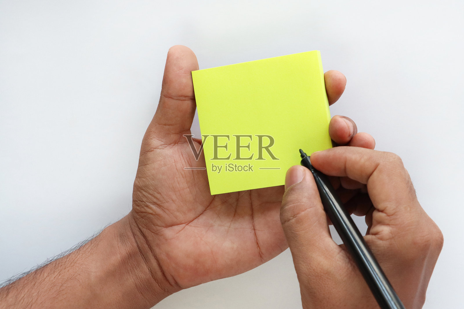 手掌中握着一张单独的黄色便签纸，无法辨认的人正在用黑色圆珠笔记录，黄色纸张方形，文具，俯视图，创意构思与思维。照片摄影图片