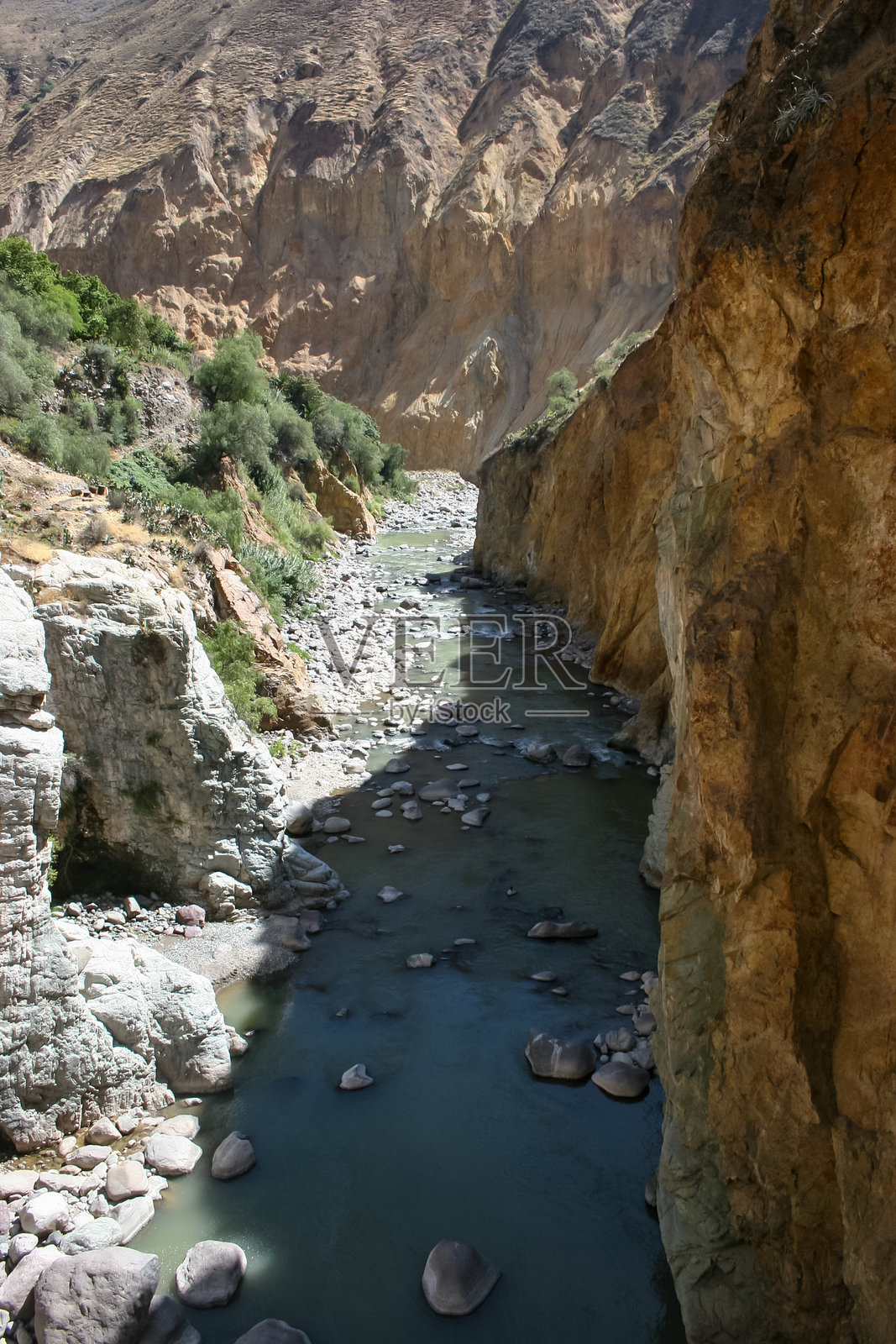 在秘鲁南部的科尔卡峡谷地区，干旱的沙漠环绕着一条流动水量不多的小溪，周围是高耸的山脉和广阔的沙漠平原，天空湛蓝。照片摄影图片