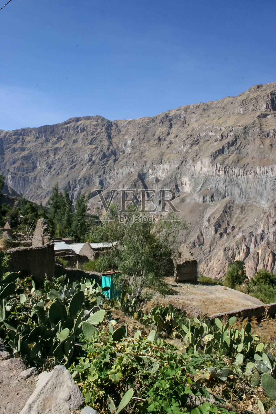 位于秘鲁南部科尔卡峡谷地区的干旱沙漠中，一个小村庄坐落在山谷里，周围是高耸的山脉和广阔的沙漠平原，天空湛蓝。照片摄影图片