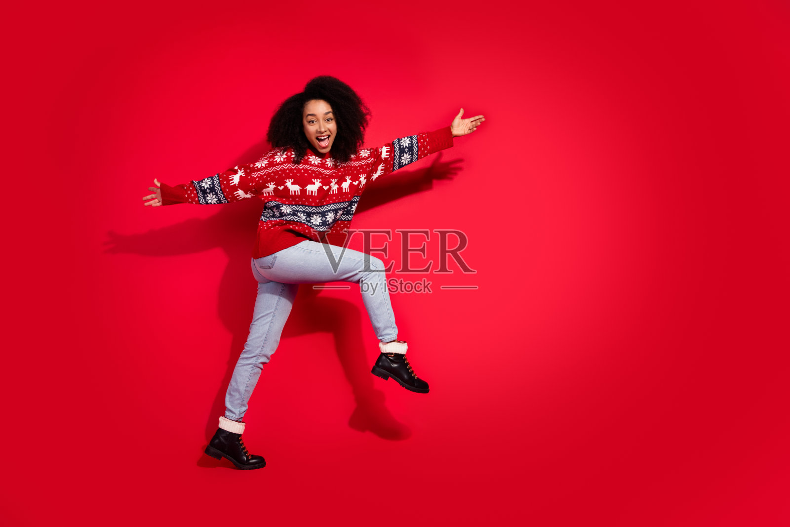 全身照，快乐的漂亮女士穿着丑陋印花毛衣，匆忙享受圣诞前夕，背景为空旷的红色。照片摄影图片