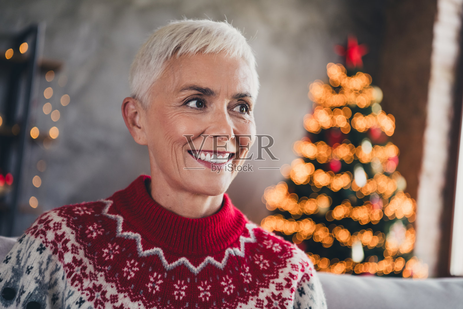 坐在沙发上的美丽老年女性幻想着新年圣诞花环灯饰，室内平静温馨。照片摄影图片