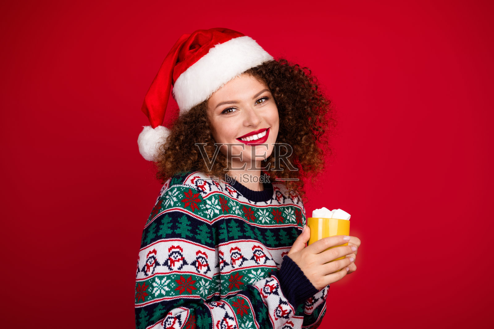漂亮年轻女性手持可可，穿着圣诞节毛衣，背景为红色。照片摄影图片