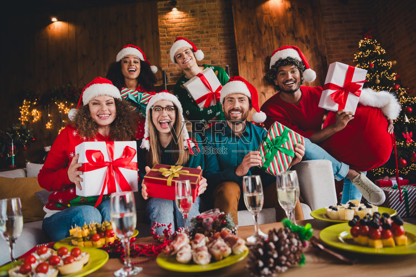 一群快乐的年轻朋友坐在沙发上，庆祝秘密圣诞老人活动，享受温馨的圣诞派对装饰，室内宽敞的公寓。照片摄影图片