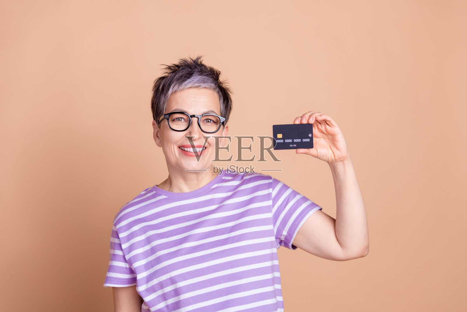 穿着条纹时尚服装的可爱女性手持银行卡，背景为米色。照片摄影图片
