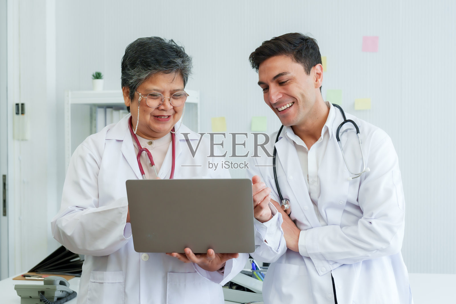 微笑的医疗专业人员、教师和实习生在明亮的诊所环境中围绕一台笔记本电脑分享时刻。资深医生与实习生在计算机发现上进行愉快的互动。照片摄影图片