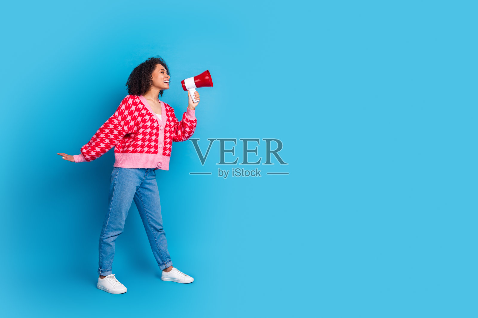 穿着红色时尚开衫的美丽美国女孩，卷发，背景为蓝色，展示信息的肖像照片照片摄影图片