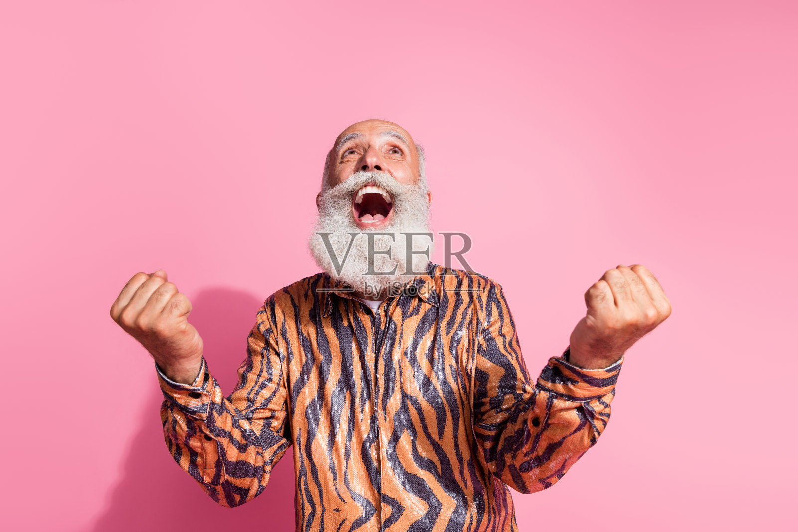 疯狂欢庆的老人仰望天空，举起拳头，穿着闪亮的衬衫，背景为柔和的色彩。照片摄影图片