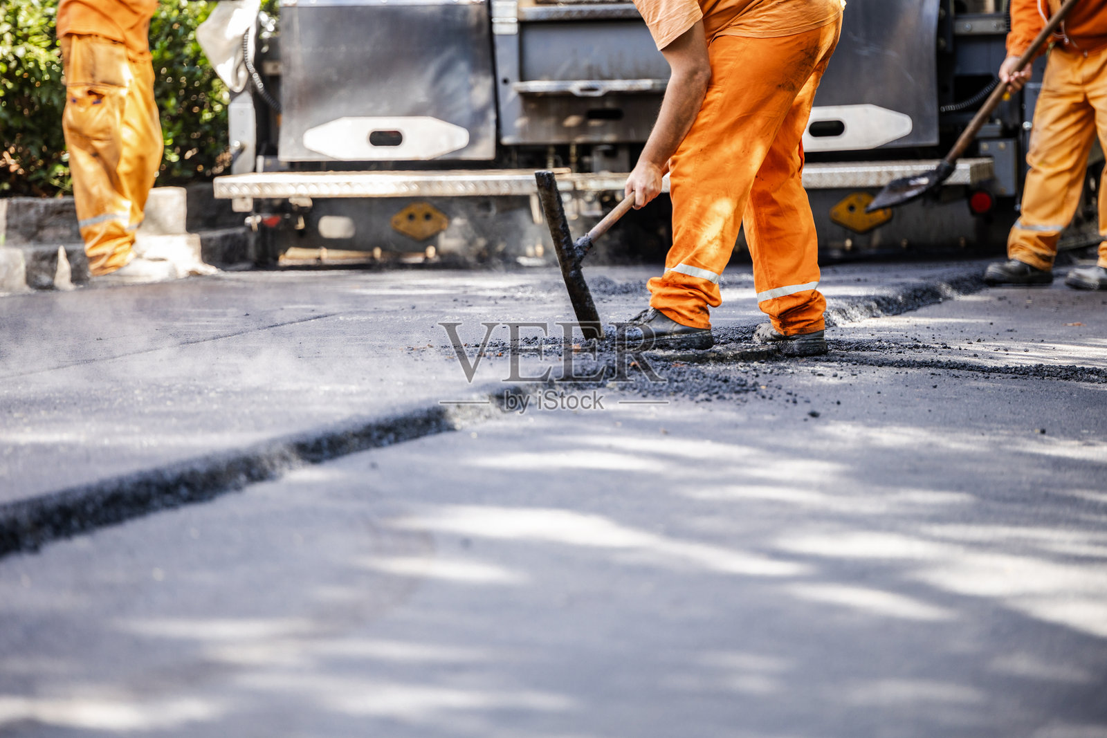 工人在城市街道上进行沥青铺设，身穿鲜艳的橙色工作服，正在白天进行施工项目。照片摄影图片