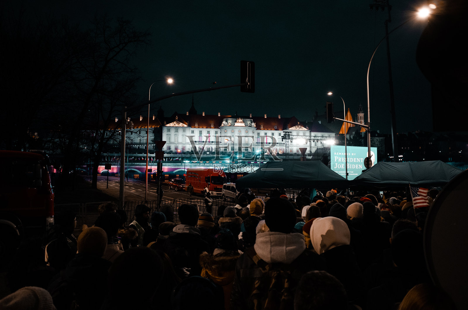 图中显示了一群人聚集在夜晚,站在一座大型亮灯建筑前。华沙照片摄影图片