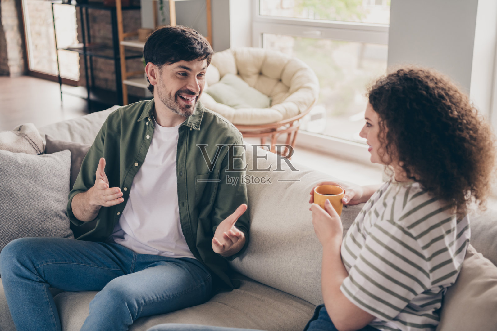 两位年轻伴侣坐在沙发上交流，喝茶，室内公寓的客厅。照片摄影图片
