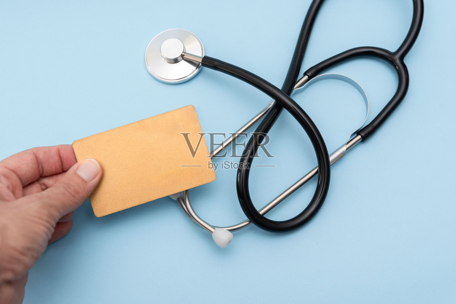 手握空白保险卡，旁边是听诊器，背景为蓝色，医疗和健康援助照片摄影图片