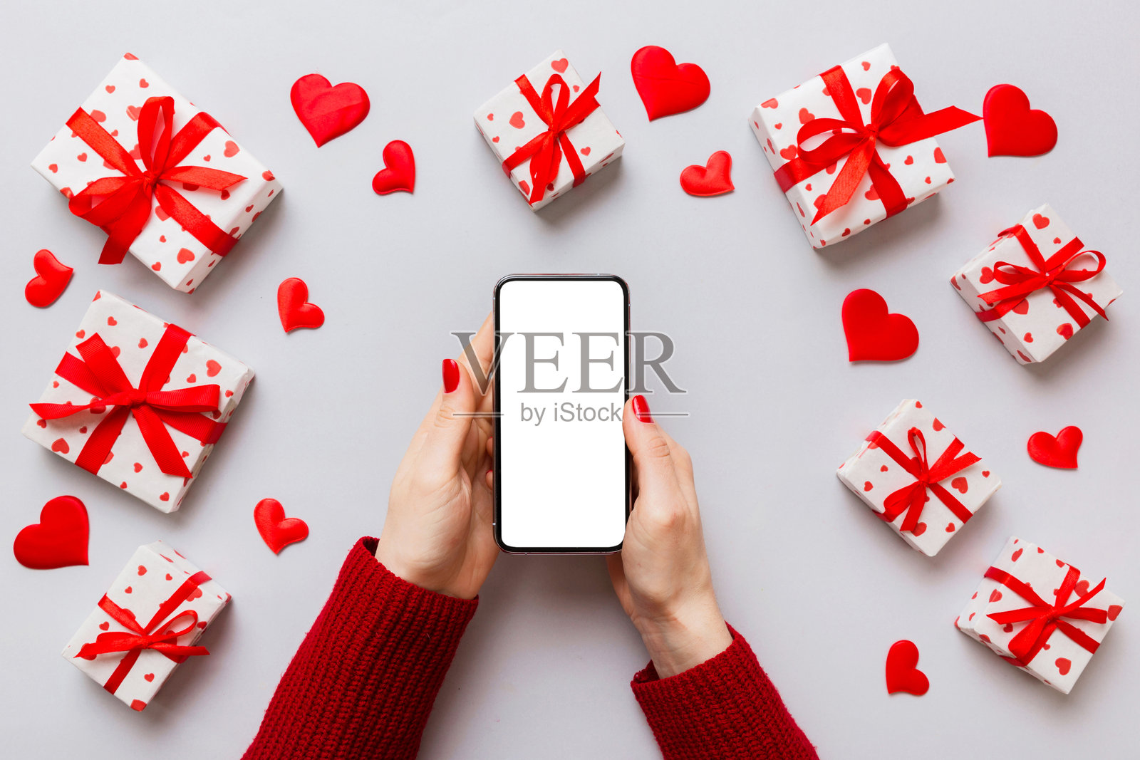 女人手持空白屏幕的手机，背景为彩色心形图案，情人节概念俯视平铺图。照片摄影图片