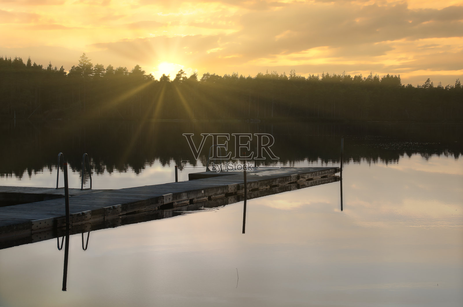 瑞典湖泊上的木栈道在日落时分。日落的倒影映在水面上。照片摄影图片